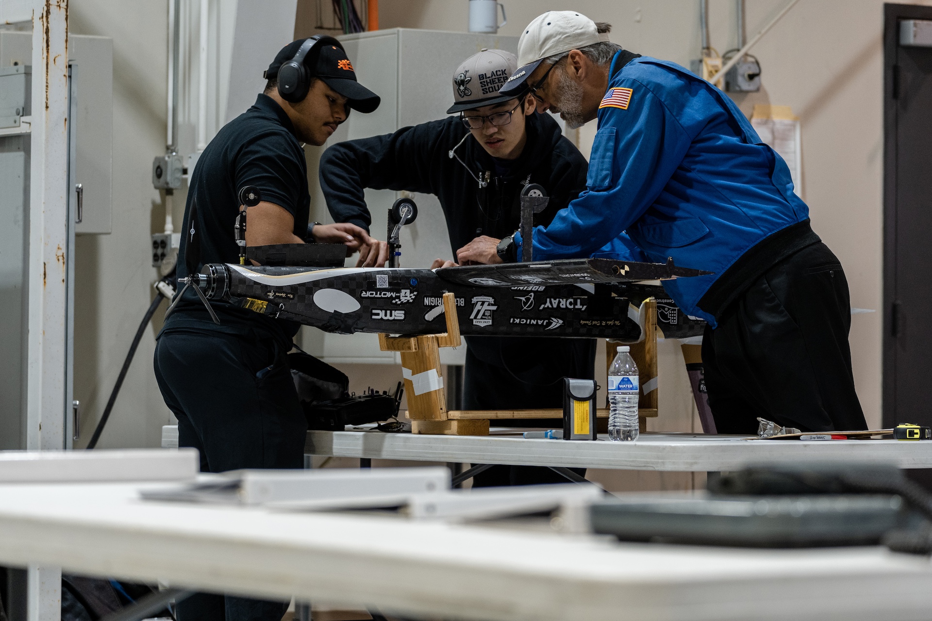 Three people adjusting a remote controlled aircraft in a stand