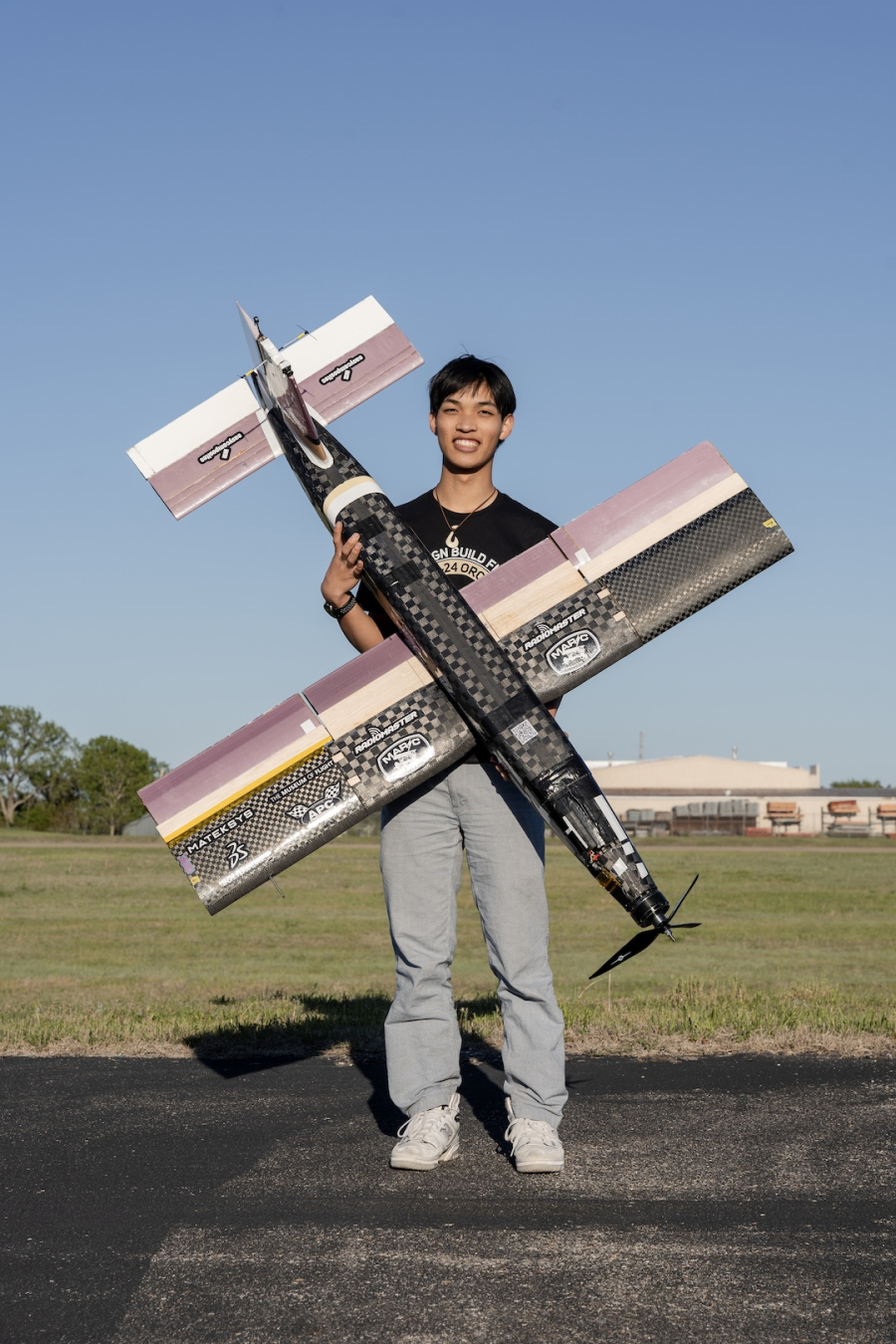 A person stands outdoors on a sunny day, holding a large remote controlled aircraft. 