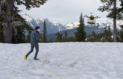 man standing on snow covered ground near a drone flying