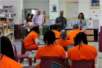 Inmates in orange prison attire looking at instructors.