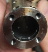 Close-up of the end of a cylindrical metallic object with a central circular opening and surrounding holes.